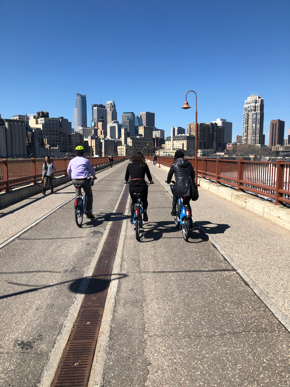 Collaboration with city leadership and national experts, including Janette Sadik-Khan, on active mobility initiatives cycling across the Stone Arch Bridge, Minneapolis riding towards downtown skyline.