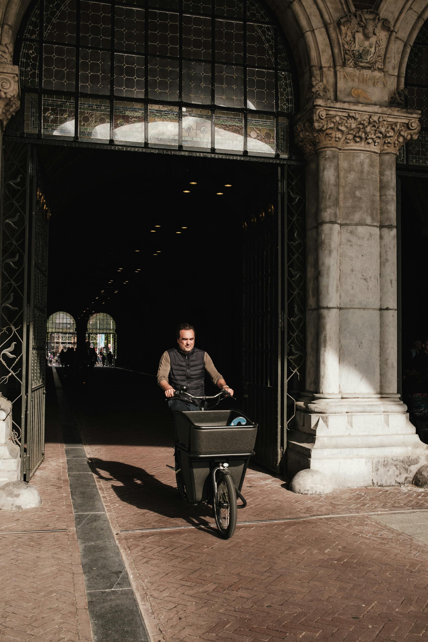 Urban cycling scene with a man on a cargo bike in a historic city alleyway.